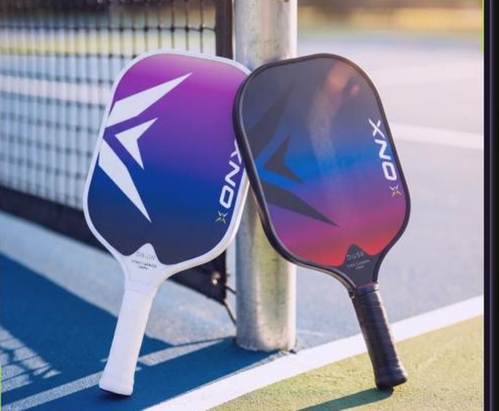 Two ONX paddles resting against a net post on a pickleball court